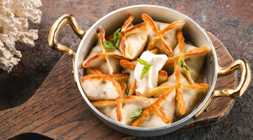 ИНГРЕДИЕНТЫ Для подачи (на 1 порцию):
перец черный молотый – 5 г
кундюбы п/ф – 140 г
растительные масло – 15 мл
бульон овощной п/ф – 50 мл
базилик зеленый – 1 г
сметана соевая – 15 г
Для теста:
мука пшеничная в/с – 600 г
крахмал кукурузный – 15 г
соль – 10 г
растительное масло – 20 мл
вода – 1 стакан
Для фарша:
растительное масло – 20 мл
гречка отварная – 1300 г
огурцы соленые – 150 г
лук пассерованный – 200 г
шампиньоны жаренные – 200 г
петрушка – 10 г
соль – 15 г
ПОШАГОВЫЙ РЕЦЕПТ ПРИГОТОВЛЕНИЯ
Шаг 1
Приготовить тесто. Просеять муку горкой, сделать в ней «колодец», добавить остальные ингредиенты и, подливая воду, замесить тесто. Скатать тесто в шар, накрыть салфеткой и оставить на полчаса.
Шаг 2
Приготовить фарш. Обжарить отварную гречку, добавить мелко нарезанные соленые огурцы, слегка припустить. Положить пассерованный лук, жареные шампиньоны и мелко рубленную петрушку. Посолить, поперчить, хорошо перемешать, снять с огня.
Шаг 3
Раскатать тесто как на пельмени, вырезав круглой формой (примерно по 5 г). Сформировать кундюбы, беря примерно по 15 г фарша на 1 шт. Поднять края теста и скрепить, чтобы получился узор в виде креста.
Шаг 4
Обжарить кундюбы на растительном масле, уложить в сотейник, добавить грибной бульон и тушить до готовности. Подавать с мелко рубленым базиликом и соевой сметаной.