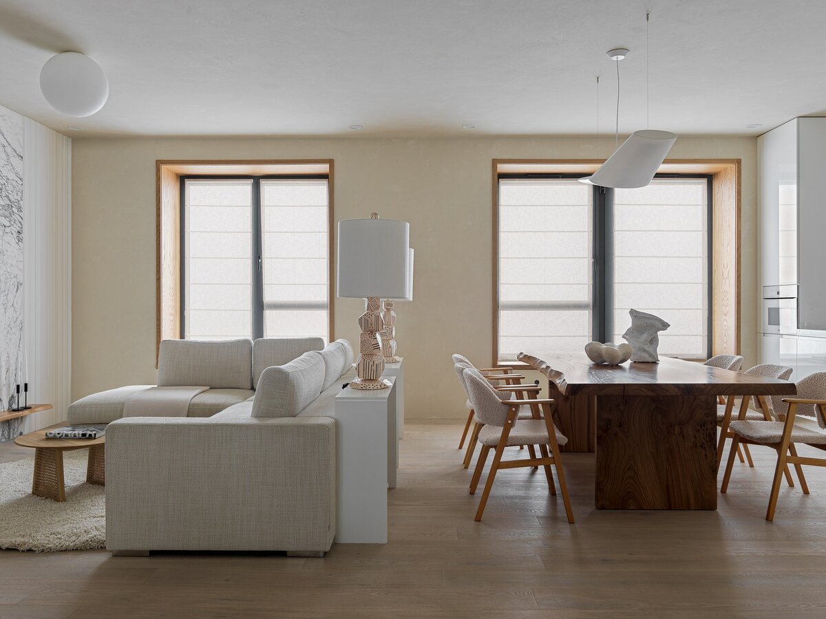 Фото: Сергей КрасюкГостиная-кухня. Диван, BoConcept; кофейный столик, HKLiving  (L’Appartement); стальные консоли за диваном, Ominimalism; потолочные светильники, Artemide; настольные лампы на консолях, Bollu; обеденный стол из слэба карагача изготовлен на заказ в WoodCraftStudio; на столе ваза “Зигзаги” (Ceramum) и скульптура “Облако” (Troubadour shop); на окнах льняные римские шторы; декоративное покрытие стен и потолка — Александр Чирков, микроцемент “Краски Бриз”; паркет, Coswick.
