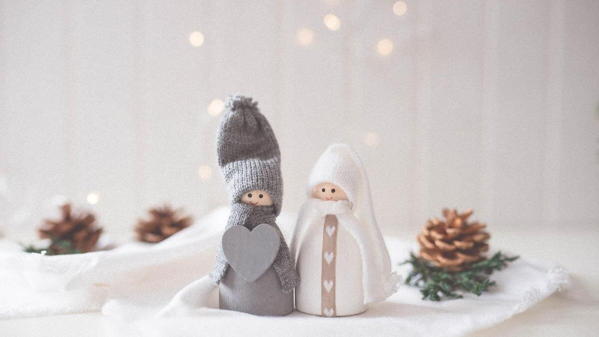    На белом покрывале стоят фигурки мальчика в сером костюме и девочки в белом костюме. Одежда на игрушках сделана из шерстяных ниток:Unsplash/Рaige cody