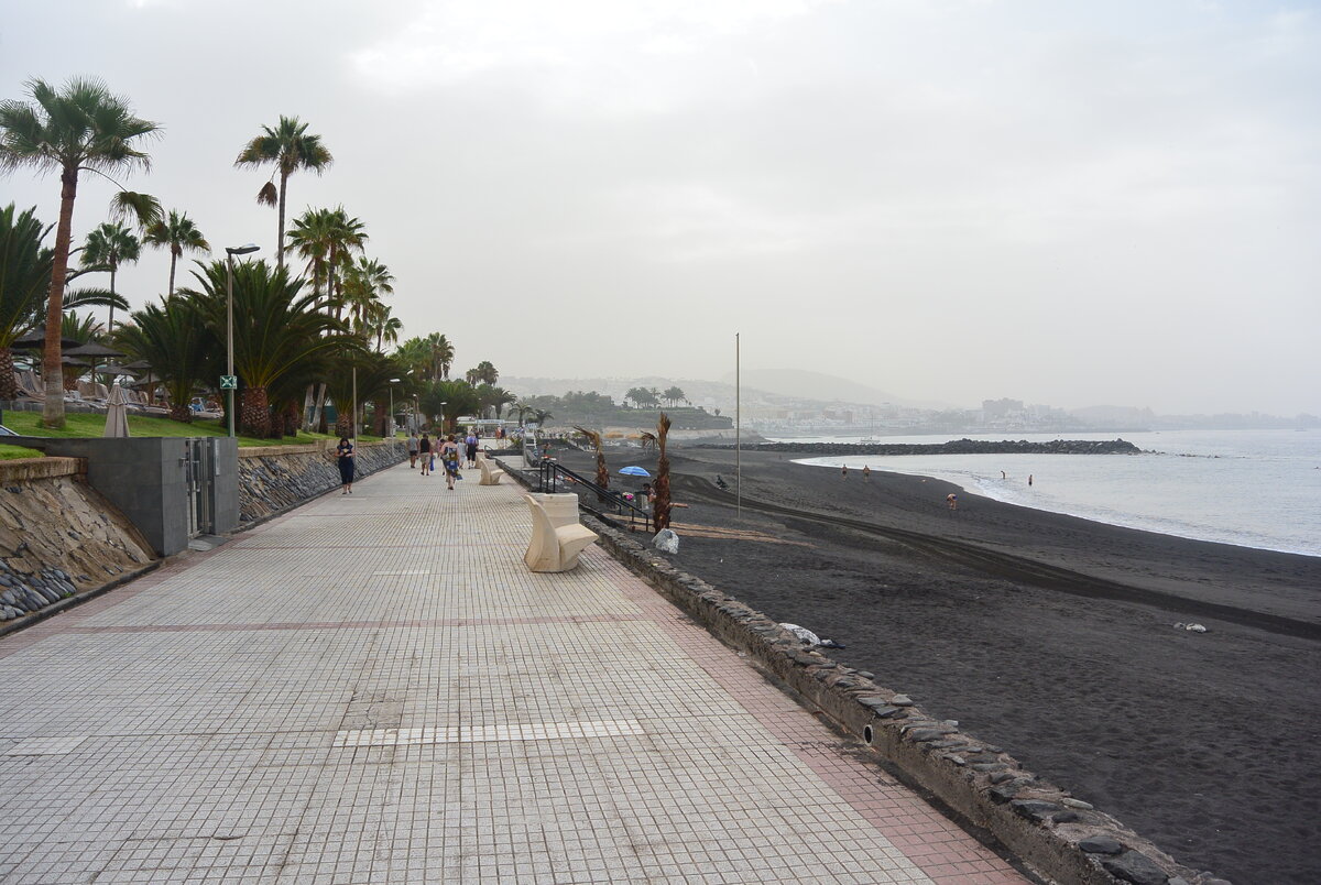 Набережная проходит над пляжем Эль Дюке. Часть пляжа покрыта черным вулканическим песком