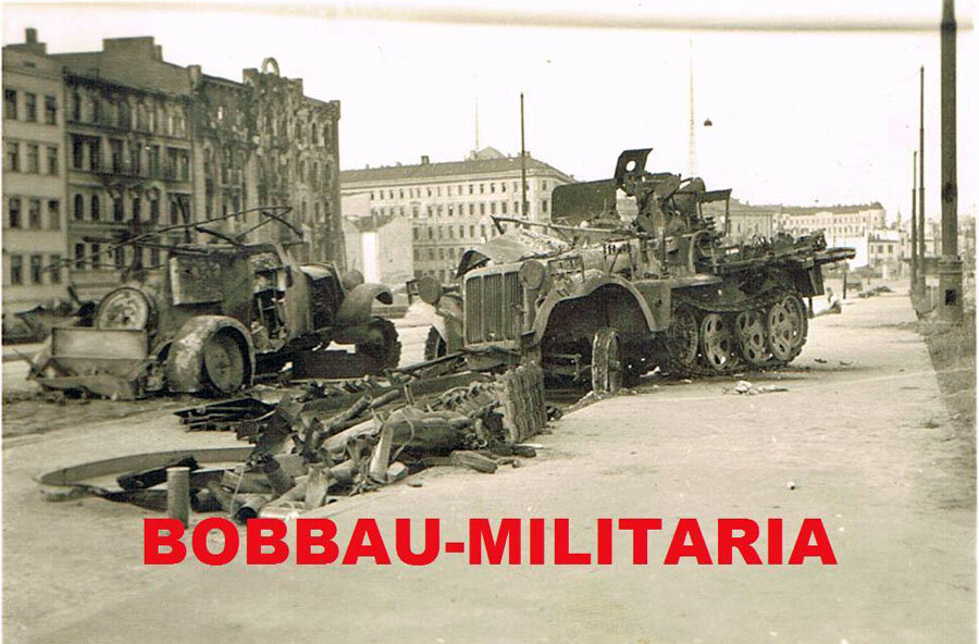 Зенитная самоходная установка на базе колесно-гусеничного артиллерийского тягача Sd.Kfz.10 на въезде на Земгальский мост, который начинался от улицы Прагас и поднимался параллельно улице 13 Января. В кадре слева видны сгоревшие дома №№ 13 и 15 по этой улице (снесены после войны) и часть уцелевшего № 17 (снесен уже в наши дни). Предположительно, это одна из трех машин из Fla-Btl.604, прорвавшихся через мост и уничтоженных советскими войсками.