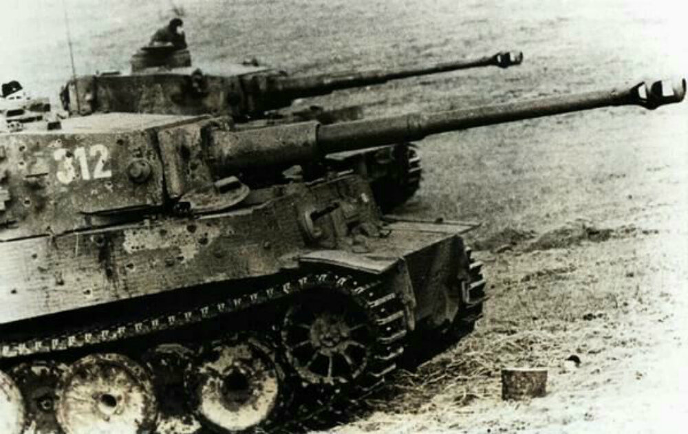 Немецкие танки PzKpfw VI Ausf. E «Тигр» в поле на Восточном фронте. На башне и борту ближнего танка видны многочисленные отметины от попаданий, сделанные, предположительно, пулями советских противотанковых ружей. Фотография использована в качестве иллюстрации.