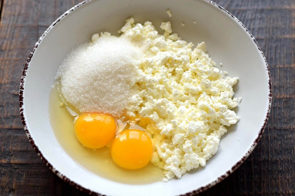 1. Зернистый творог уложите в глубокую емкость, вбейте два яйца.
Всыпьте необходимое количество сахара.