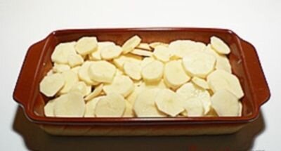     Картофель моем щеткой под проточной водой. Складываем в кастрюлю, заливаем водой и варим до готовности минут 30-40. Когда картофель в мундире будет готов, сливаем воду и даем ему остыть. Остывшую картошку очищаем и нарезаем кружочками в 0,5 сантиметра. Форму для запекания смазываем жиром и выкладываем порезанный картофель. Посыпаем солью, перцем и измельченным шалфеем.       