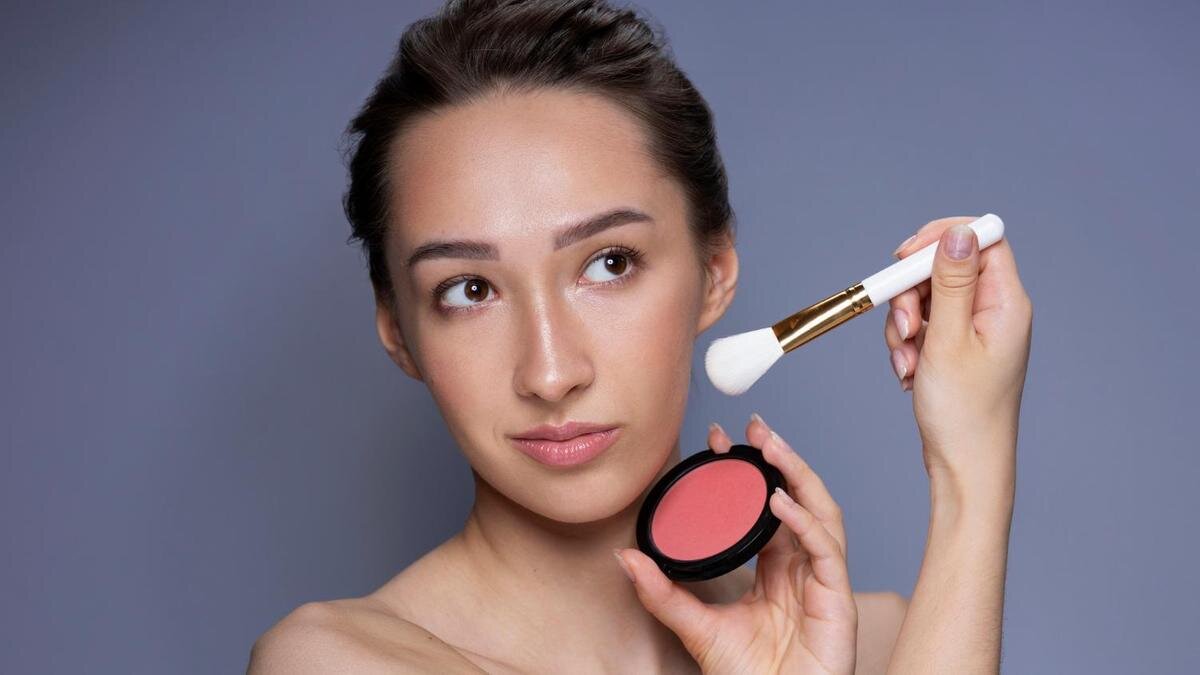    Девушка держит румяна и кисть возле лица:Freepik