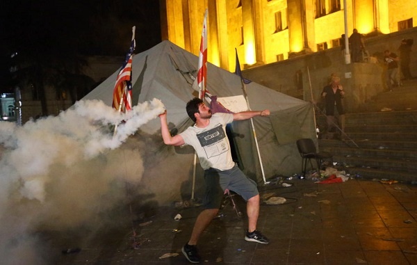 Участник акции протеста бросает дымовую шашку в полицейских