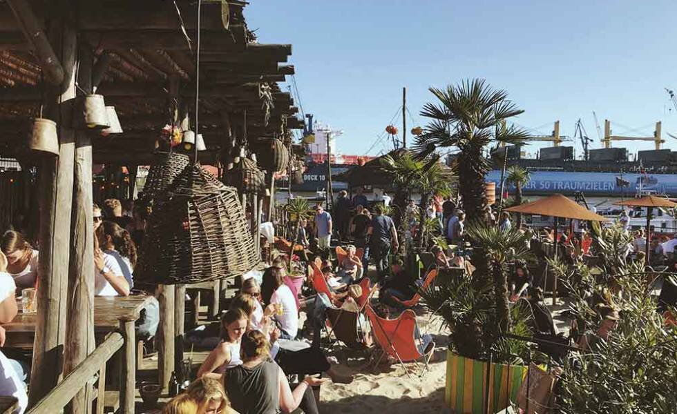 Терраса пляжного бара StrandPauli в Гамбурге с портовыми кранами на заднем плане. STRANDPAULI.DE