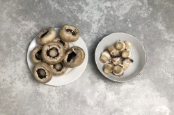 Грибы аккуратно помойте под проточной водой. Не надо полностью опускать их в воду, они как губка, впитают жидкость и станут водянистыми. Лучше смыть грязь губкой. Затем с помощью ножа отделите у грибов ножки, стараясь не сломать шляпку. Достаточно легко подрезать по кругу и отломить ножку рукой.