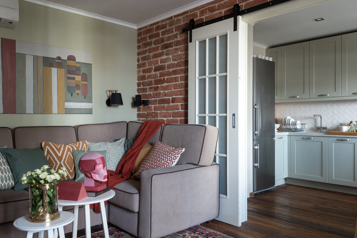 Листайте галерею. Покраску сочетали с лофт-отделкой. Отдельные участки облицевали плитами, которые нарезали из настоящего кирпича. Пол уложили паркетной доской. Ее текстура сочетается с фасадами мебельной конструкции, выстроенной вокруг ТВ-зоны.