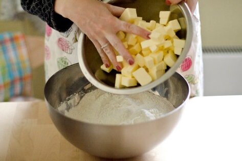 В муку выкладываем нарезанное на кубики сливочное масло. По рецепту основа ватрушки с творогом имеет рассыпчатую структуру. Поэтому важно, чтобы все используемые продукты были изначально холодными. Лучше перед замешиванием теста песочного для творожного пирога подержать их на холоде.

В муку перекладываем нарезанное кубиками масло.