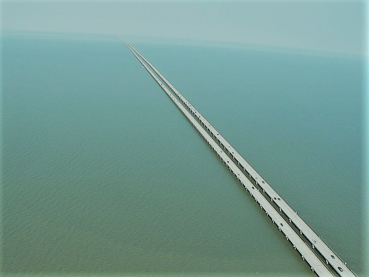 Мост уходит далеко к горизонту. Каждое из двух его дорожных полотен имеет по две полосы. Вдалеке можно увидеть волнорез, выступающий за пределы основных полос. 