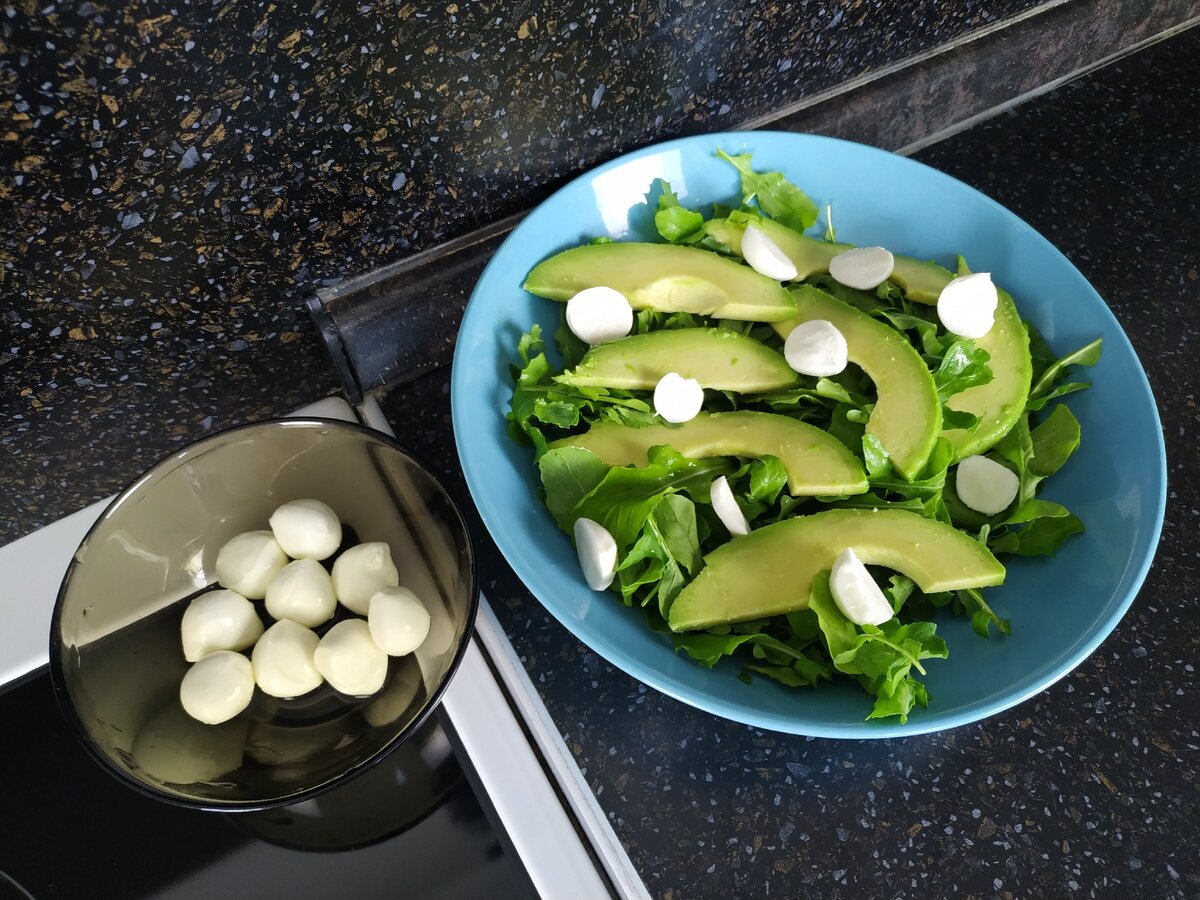 Рукколу вымыть, выложить на тарелку, добавить авокадо. Из пачки шариков моцарелла слить жидкость, шарики разрезать пополам, добавить в тарелку.