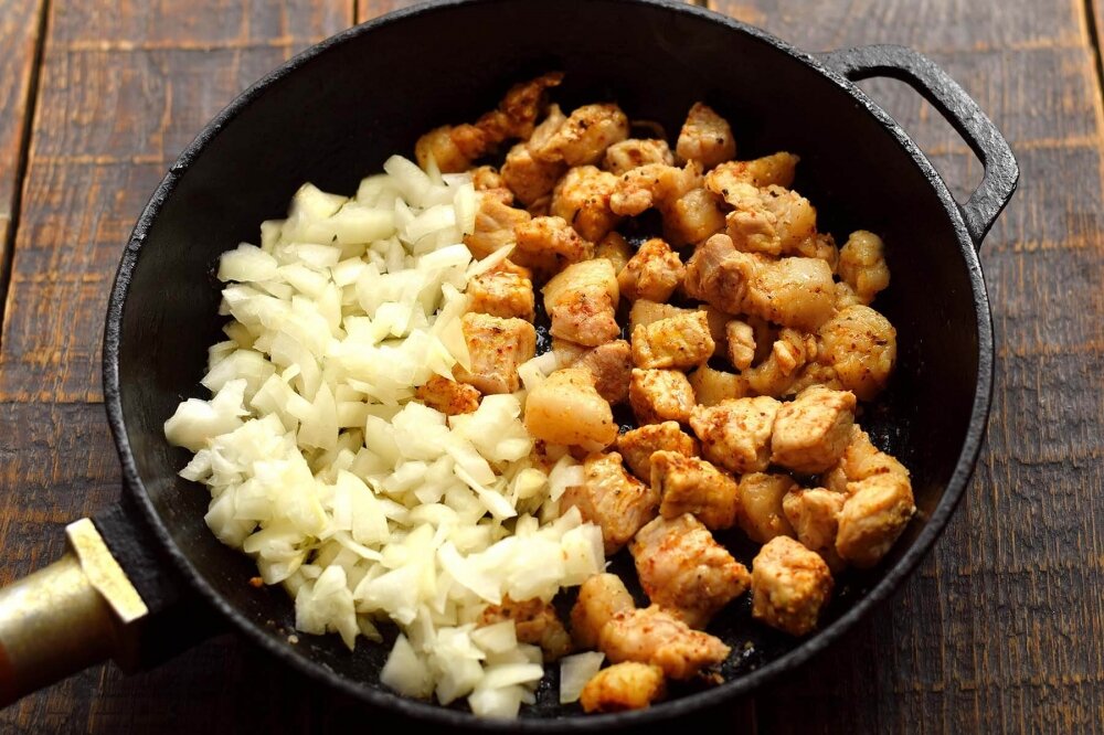 1. Мясо ополосните, нарежьте на куски среднего размера. На огонь установите сковороду, влейте растительное маслом, разогрейте, после закиньте мясо. Жарьте мясо на сильном огне 5-8 минут до полного испарения жидкости, периодически перемешивая его лопаткой. Головку лук очистите, нарежьте мелким кубиком, добавьте к мясу, перемешайте.