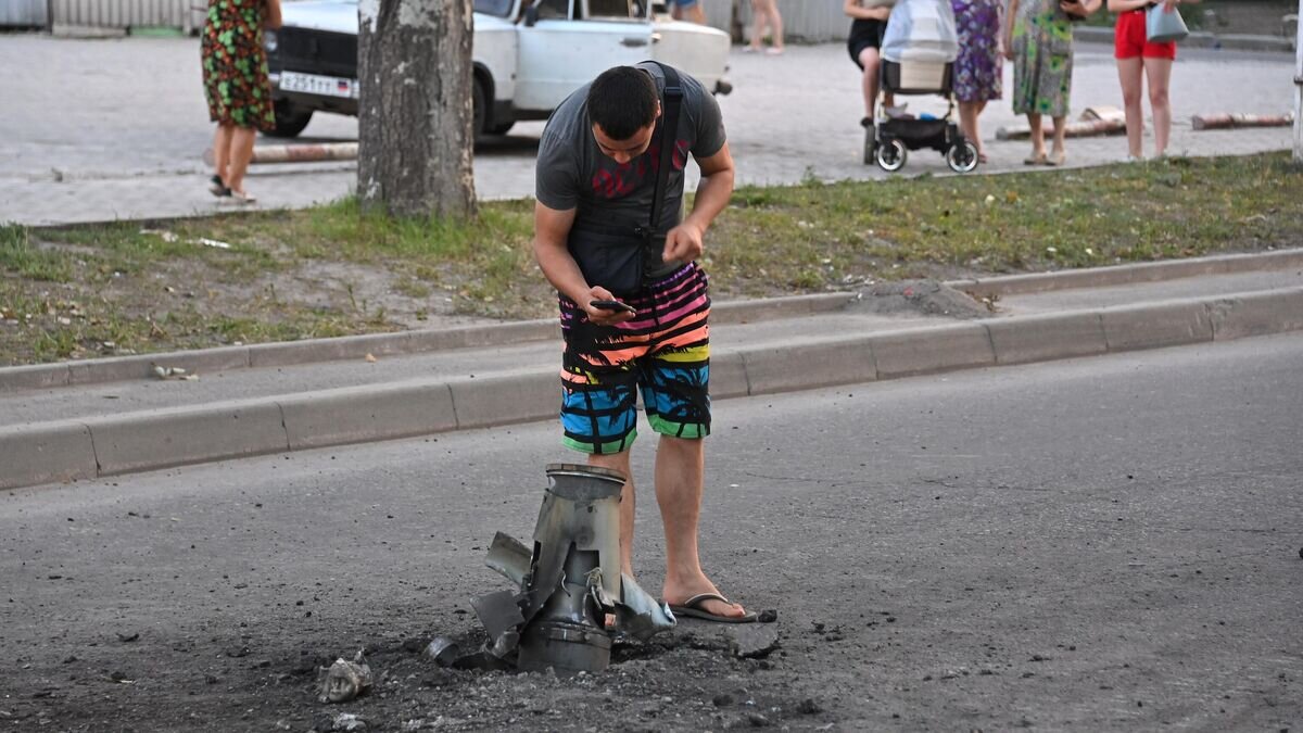    Жители города около неразорвавшегося боеприпаса на месте обстрела Ленинского района Донецка© РИА Новости