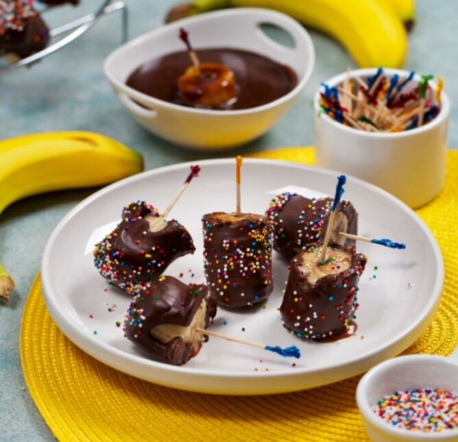 Банановый десертИнгредиенты:бананы — 5 шт.шоколад — 100 гцветная посыпкаПриготовление:Разрезать бананы на кусочки. Шоколад растопить на водяной бане.Окунуть кусочек банана в шоколад и присыпать цветными украшениями или молотыми орехами.Оставить в холодильнике, пока не застынет шоколад.