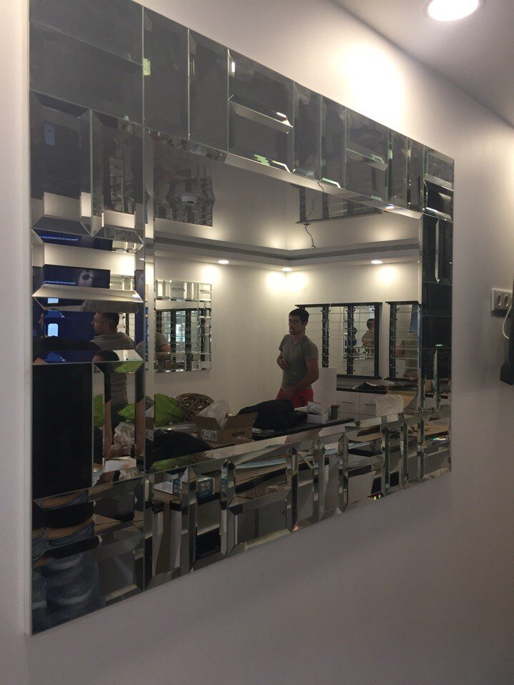 Панно, украшающее прихожую, спальню или другое помещение, составленное из отражающих деталей, является эксклюзивным видом настенного декора. Данное решение может превратить скучную комнату в неповторимое арт-пространство. Зеркала с присущим им блеском, создают волшебную атмосферу, которая расслабляет и успокаивает. Техника по получению таких изделий очень разнообразна, поэтому эффектные изделия для обустройства стен красиво смотрятся как в модных, так и в классических стилях интерьера.
Использование в интерьере
Изделия с отражающей поверхностью в дизайне помещений активно применяются декораторами для моделирования пространства и упрощения задач оформления. Эксклюзивный отражающий эффект зеркального панно дает возможность легко выполнять коррекцию любых недостатков в коммерческих и жилых помещениях:
- изменять вид малогабаритных и узких помещений благодаря визуальному увеличению пространства;
- улучшать качество света и рассеивать его по всей комнате;
- делать маленькие помещения более глубокими и объемными при установке фальш-окон или ширм с зеркальным панно;
- делать потолки выше в зрительном восприятии за счет использования вертикального панно на стенах, которое состоит из большого количества плиток в форме ромбов. Лучше всего если раскладка будет диагональной или от низа к верху будет переходить от больших к маленьким элементам;
- возможна компенсация минусов габаритов в ванной, гостиной или прихожей для монтажа большого зеркала, ведь панно, особенно с фацетом – это лучшая альтернатива в данном случае.
При помощи отражающих элементов можно не просто моделировать помещение, но также нетривиально создавать акцентные стены в доме. Такой эффективный дизайн всегда красиво и изысканно смотрится в гостиной, спальне, на кухне, особенно если панно из зеркала оснащено подсветкой и располагается рядом с камином. Можно наблюдать за красивой игрой света в моменты отдыха или занятия домашними делами.
Благодаря использованию таких изделий легко решает проблема с недостатком света. Мастера нашей компании могут выполнить монтаж панно в комбинации с осветительной системой. Так в помещении будет царить волшебная атмосфера.
Зеркальное панно прекрасно сочетается с любым интерьером. Даже строгие стили идеально сочетаются со сложными зеркальными изделиями, выполненными в соответствии с модными тенденциями. В мастерской работают опытные профессиональные сотрудники, имеющие большой опыт проектирования помещений. Они смогут выбрать оптимальный размер, форму и состав зеркального панно, чтобы он наиболее точно соответствовал вашему интерьеру.
Основываясь на ваши личные предпочтения и пожелания, мы предложим изделия из портфолио или создадим для вас индивидуальное панно. Особенно панно из зеркальных элементов в интерьере подходит для жилища творческих и оригинальных личностей.