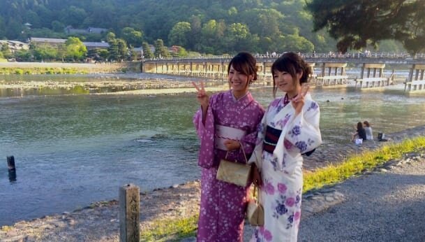Одетые в кимоно японские туристы позируют на фоне моста Тогэцуке Арасияма