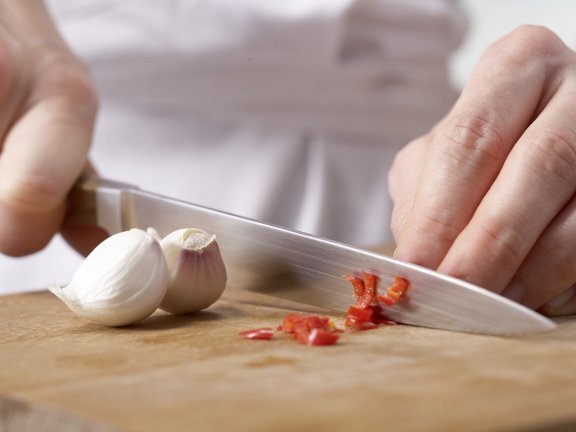 Перец чили разрежьте пополам, удалите семена. Перец промойте и мелко нарежьте. Очистите чеснок и измельчите.