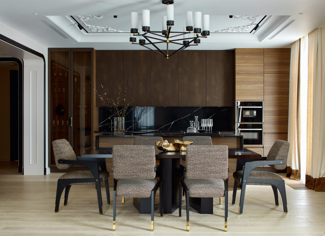 Кухня и столовая зона гостиной. Фасады кухонного гарнитура облицо­ваны шпоном ореха, а отделка верхних шкафчиков имитирует ржавчину. Витрина сделана на заказ; стол по эскизам Полины Пидцан, Gaisin & Co; стулья, InsidherLand, обиты тканью, Misia; люстра, Visual Comfort & Co., посуда и стекло из Galerie 46; шторы сшиты из ткани, Dedar.