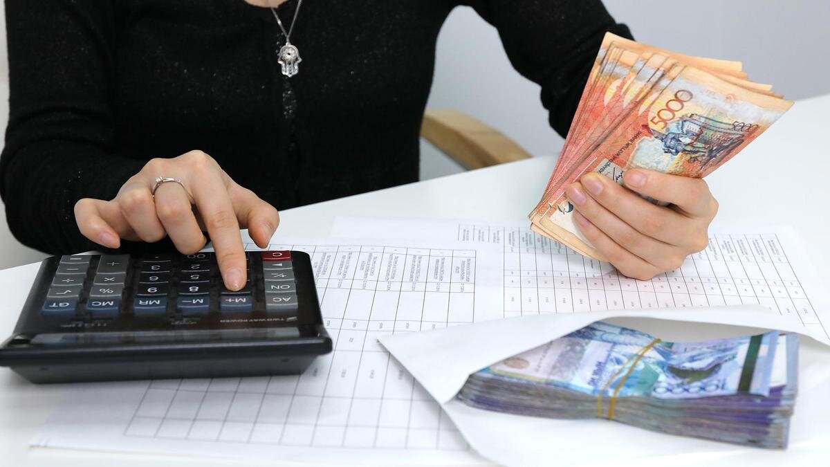    Женщина считает деньги с помощью калькулятора:NUR.KZ/Петр Карандашов