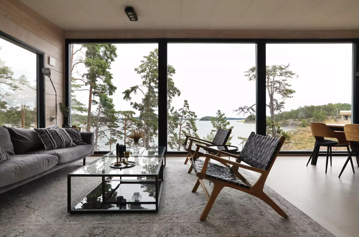 Начнем экскурсию с гостиной. Это самое эффектное место в доме благодаря сплошному остеклению и виду на озеро. Мебель и прочие предметы подобраны в нейтральной цветовой гамме — супругам не хотелось, что вещи перебивали роскошную природную панораму