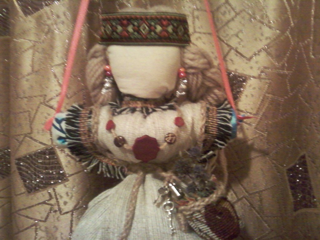 Оторочка рукавов бахромой словно крылья ангела. На груди колье-оберег, серьги-совушки - дают мудрость в решении жизненных ситуаций. Ключики  на  счастье  и  удачу, замок - на  крепкий  дом  и семью, а  в сумочке  обереговые  травы  (чертогон (чертополох). Кукла сшита в период новолуния.