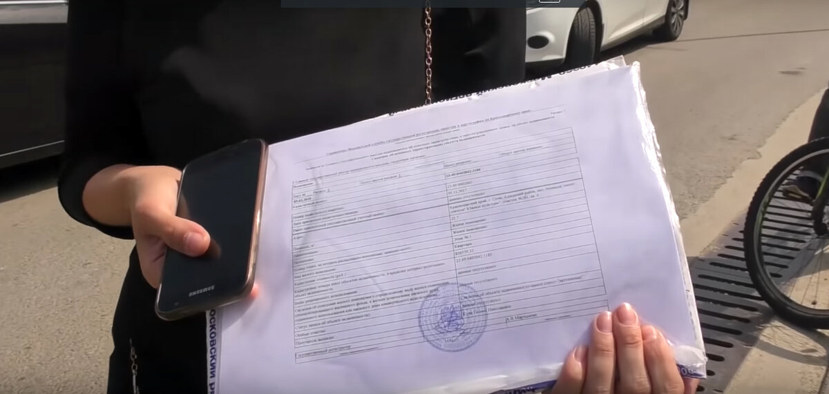 Женщина показывает свою выписку из Росреестра на квартиру, но ее никто не слушает