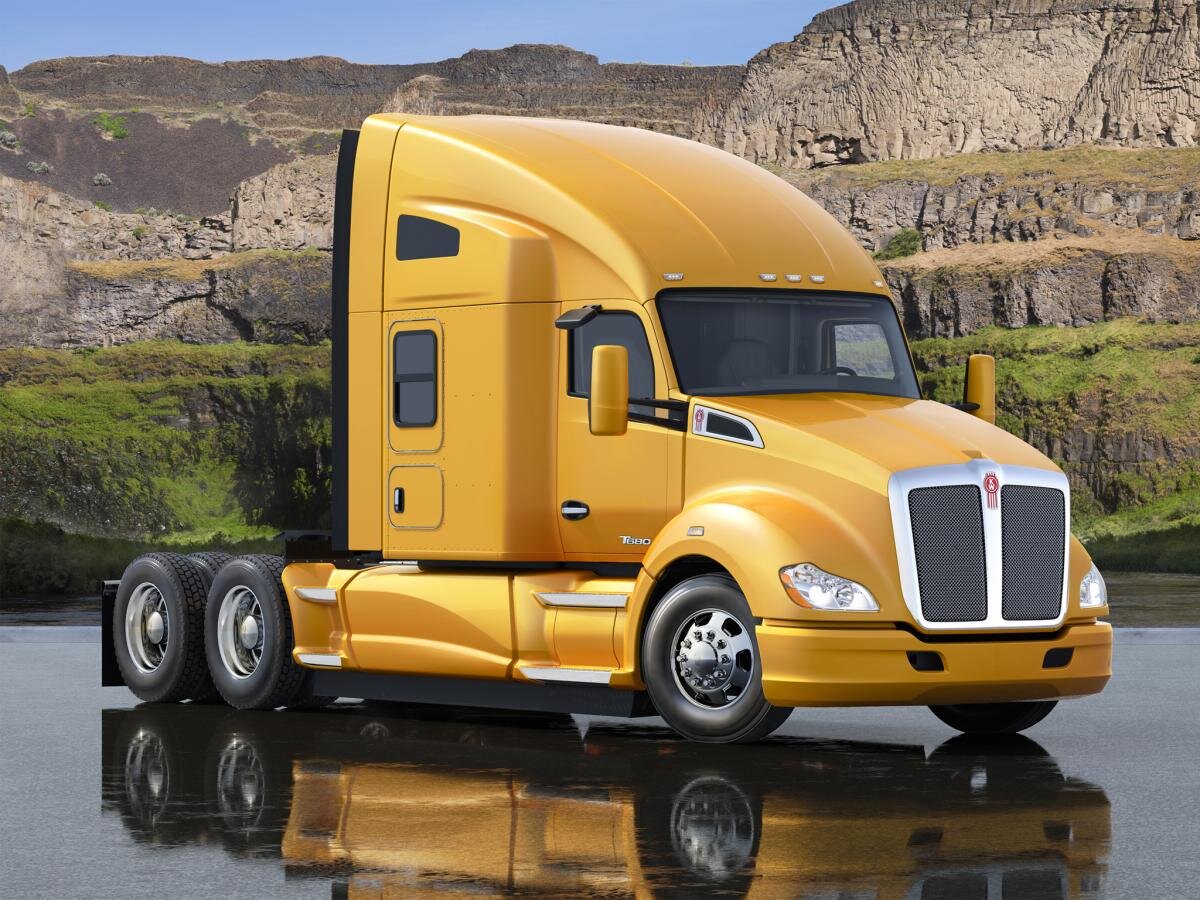 Начнем с того, что Kenworth T680 – лучший на сегодняшний день грузовик данной марки с точки зрения совершенства аэродинамики: он словно новогодняя елка обвешен со всех сторон всевозможными спойлерами. Эти улучшающие обтекаемость устройства размещены под передним бампером (составляя с ним единое целое) и по бокам рамы (так называемая «юбка»), а те, что установлены сверху и за боковинами кабины снижают аэродинамическое сопротивление полуприцепа. Причем у модификаций, предназначенных для работы на протяженных маршрутах, задние спойлеры составляют со спальным отсеком единое целое, попутно увеличивая внутреннее обитаемое пространство. На улучшение аэродинамики работают покатый капот, сильно скругленные передние крылья, обтекаемые зеркала заднего вида, зауженная кабина, а также слегка заваленные назад облицовка радиатора и ветровое стекло. Из всего вышесказанного можно сделать вывод, что Kenworth T680 разработан исключительно для магистральных перевозок: даже у модификации с короткой, так называемой «дневной» кабиной над ее крышей и по бокам могут быть установлены аэродинамические обтекатели, по размерам не уступающие таковым у модификаций со «спальниками». Но, все же, если перевозчику предстоит работать, к примеру, с открытым бортовым полуприцепом, полуприцепом-цистерной или полуприцепом-тралом, Kenworth T680 допускается заказать и без них.