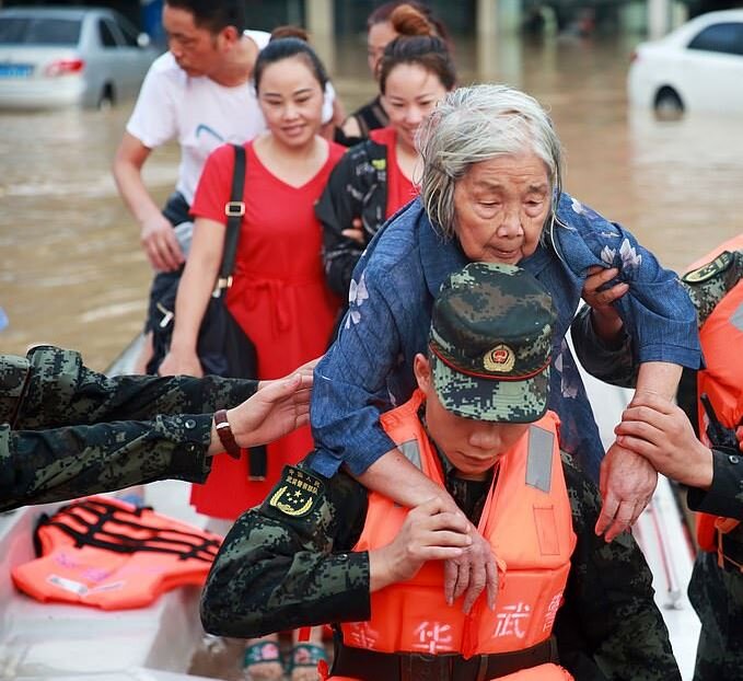 Спасатели используют лодку, чтобы эвакуировать пожилую женщину и доставить ее в безопасное место на затопленной улице, вызванной проливным дождем.