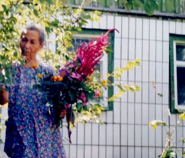 Фотокартина из архива автора. Мама с букетом на фоне родного дома.  2003 год  