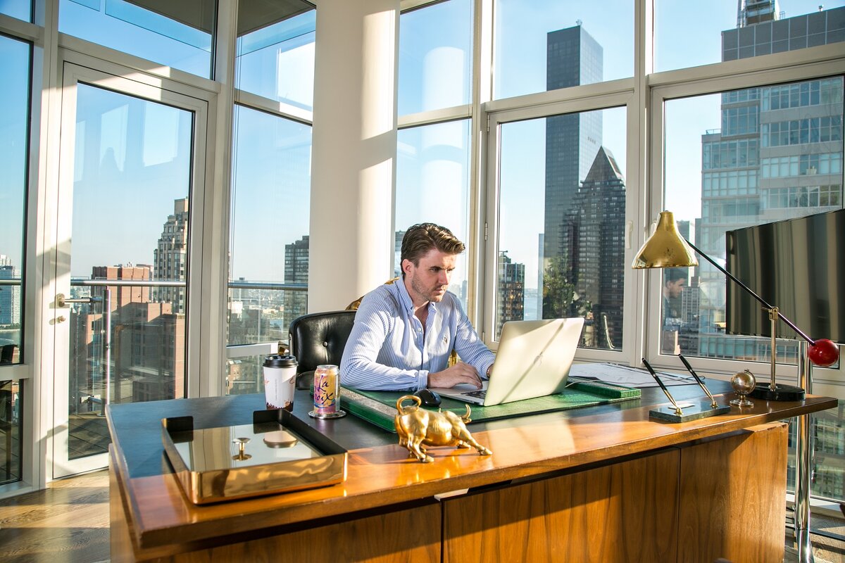 New York office of Sam Ovens, who is sitting at the table with his laptop and focusing on his tasks