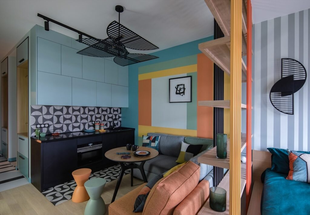 В квартире всего одно окно и планировка студии, поэтому дизайнеру пришлось продумать как будут раздеты функциональные зоны. Для этой цели между зоной спальни и кухни-гостиной был построен стеллаж. Он визуально разделяет функциональные зоны, но при этом пропускает дневной свет.