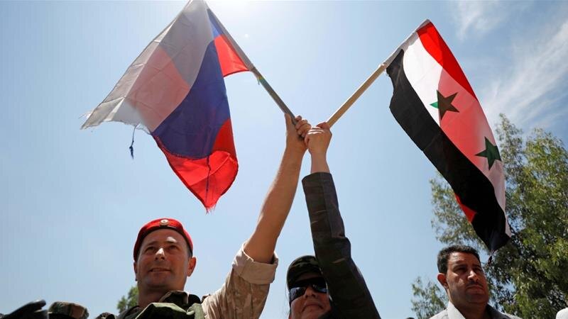 Российский солдат развевает флаг с сирийской женщиной во время открытия дороги между Хомсом и Хамой в Растане 6 июня 2018 года.