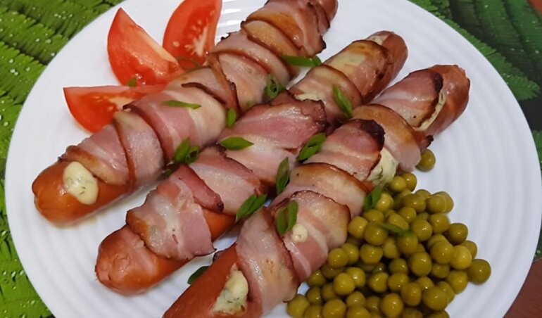 Очистите сосиски от оболочки и надрежьте каждую из них. Твёрдый сыр нарежьте соломкой. Нафаршируйте сосиски сыром и оберните одним или двумя ломтиками бекона. Отправьте в хорошо разогретую духовку на 5–7 минут. Перед подачей смажьте дижонской горчицей или любым другим соусом для мяса.