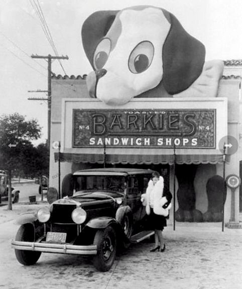 Ок. 1930 г. Женщина в шубе, позирующая рядом с ранней моделью автомобиля с Barkies Sandwich Shops No. 4 на заднем плане.