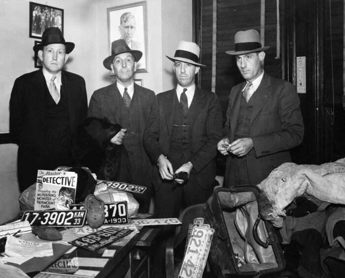 Слева направо — Смут Шмид, Эд Кастер, Тед Хинтон и Боб Элкорн (перед полицейскими разложены автомобильные номера и вещи, найденные в брошенной около городка Сеуэрс машине бандитов)