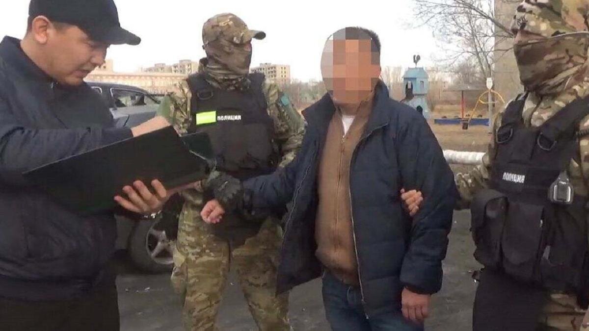    Двое сотрудников полиции в экипировке держат за руки мужчину:polisia.kz