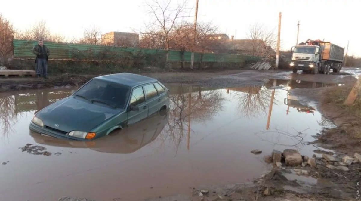  Как то в середине 90-х годов случилось мне ехать с товарищами из Мариуполя в аэропорт Борисполь. Трасса была вполне приличной. Где то на середине дороги, ночью въезжаем в село. К сожалению не помню названия села. Село располагалось в низине и по середине стояла огромная лужа. Около километра трассы было в этой луже.  Бросилось в глаза , что лужа хорошо освещена и большое количество людей , снующих , как по луже, так и вокруг нее.   Останавливаемся перед лужей. К нам подходит человек. Предлагает помочь за довольно большую цену переехать лужу. Мы решили ехать сами. Немного проехав по луже наш автомобиль сел в какой то яме. Поняли, что сами не выберемся.   Этот человек снова подходит к нам и снова предлагает помощь, но цена за услугу теперь в несколько раз больше. Мы расхохотались
  Моментально у нашего автомобиля собралась толпа мужиков в болотных сапогах. Машину приподняли вместе с нами и вытащили из ямы. Нам сказали, чтобы мы следовали вот за этим парнем и выполняли все его указания. Поехали за этим парнем, выполняя все его указания. Благополучно переехали лужу. Отметили хорошее знание нашего «лоцмана»  «лоции» лужи.
   Остановились. Наблюдаем за событиями, происходящих в этой луже. Несмотря на ночь, автомобилей по луже двигалось достаточно много и впереди каждой машины шел «лоцман». Лужа хорошо освещалась. Вокруг лужи «инфраструктура» , множество  торговых ларьков. Местный мужик поведал нам, что лужа образовалась давно, что местные жители препятствуют ликвидации лужи т,к. село кормится с нее.
  Нет мы не смеялись над жителями этого села. Мы понимали их. В России в эти «святые годы» очень многим тоже жилось не сладко и что то подобное могло быть.
  Хочется отметить доброжелательное отношение украинцев к нам. Нынешние отношения тогда могли лишь присниться в кошмарном сне
