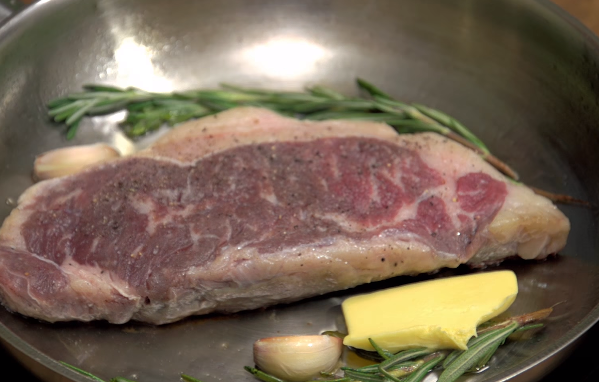 По истечению 1 минуты, к мясу добавить розмарин, чеснок и кусочек сливочного масла. Во время жарки нужно поливать мясо растопленным маслом - оно передаст все запахи (чеснока и розмарина).
