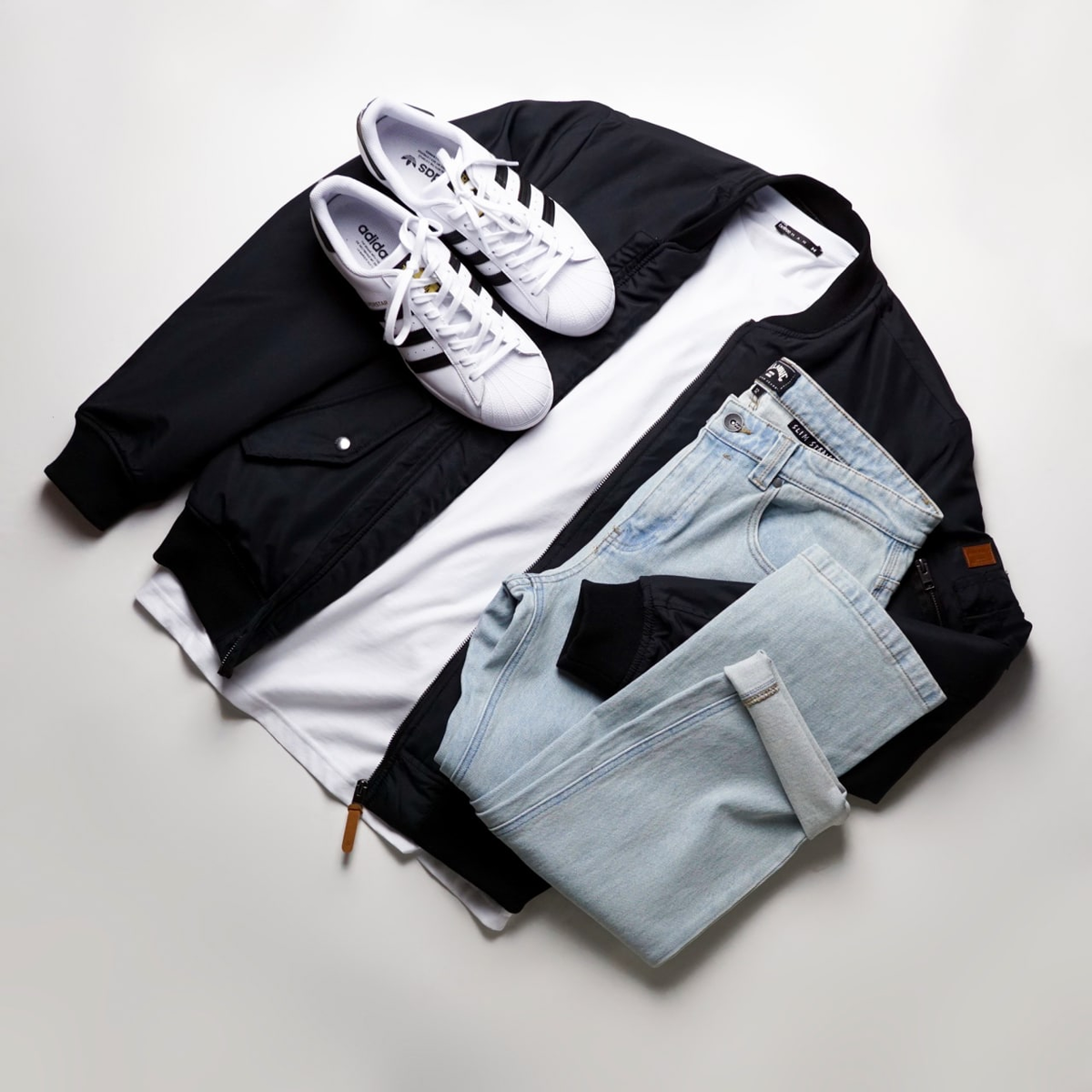 Образ с черным бомбером, светлыми джинсами и кедами Adidas Superstar.