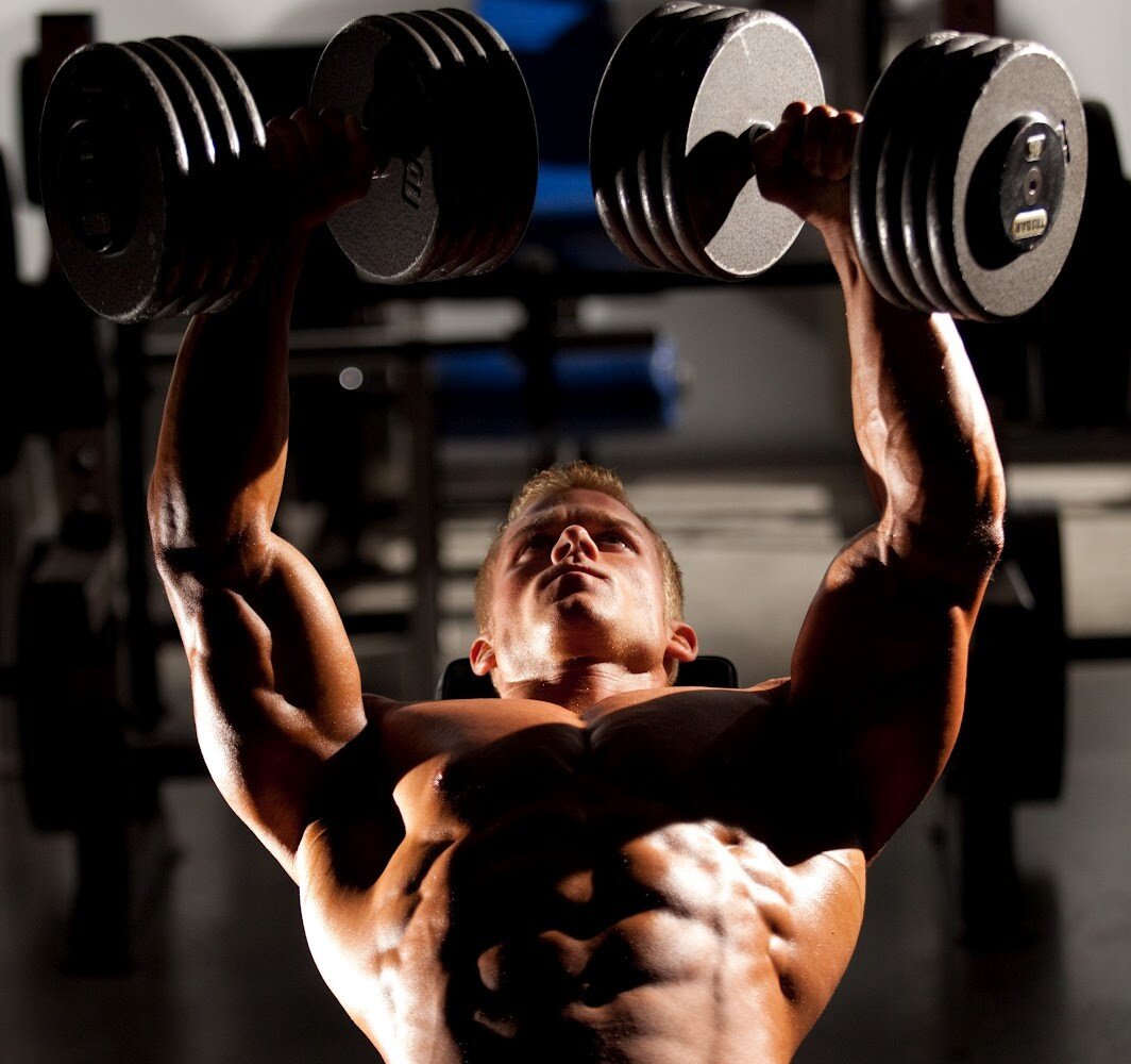 Тренировка натурала. Парень в спортзале. Гантели в зале. Спортсмен в спортзале. Мужчина в тренажерке с гантелями.