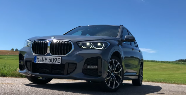BMW X1 PHEV 2020 года: вид спереди и сбоку с включенными диодными передними огнями.