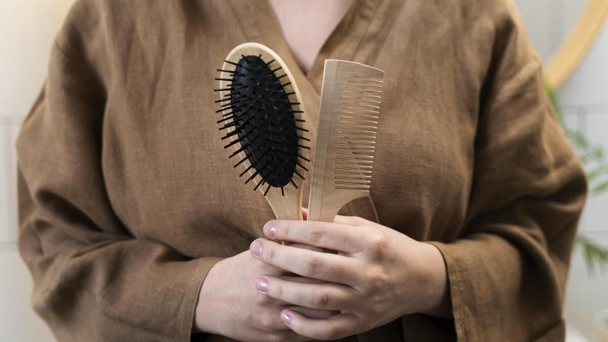    Женщина в халате держит в руках массажную щетку и деревянную плоскую расческу:Freepik