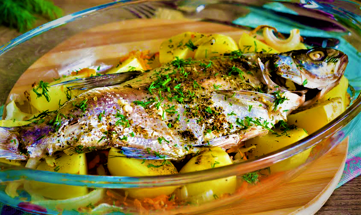 Запеченные рыба и картофель в сервировочном блюде перед подачей нас тол.