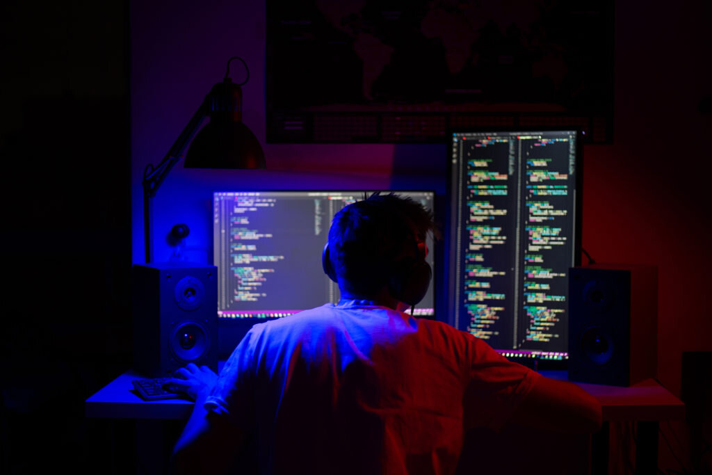    A man sits at a computer in a room at a table at night with blue lighting and programs indoor Анастасия Никифорова