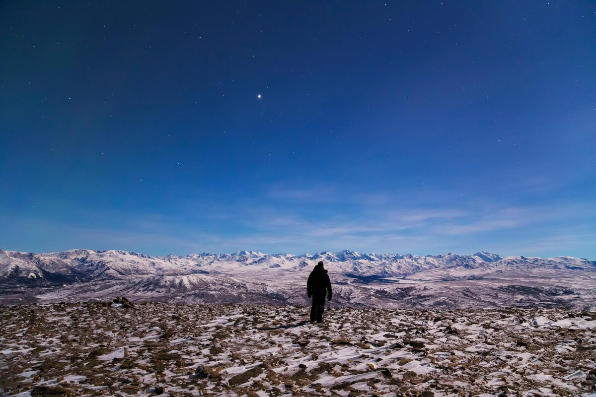    Человек смотрит на Аляскинский хребет с вершины Купола Доннелли лунной ночью. В небе ярко светится Юпитер., фото: Design Pics Inc / Alamy