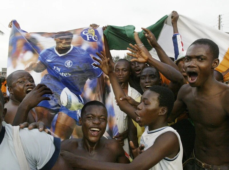 ИВУАРИЙСКИЕ БОЛЕЛЬЩИКИ ПРАЗДНУЮТ ПОБЕДУ С ПЛАКАТОМ ДИДЬЕ ДРОГБА В АБИДЖАНЕ ПОСЛЕ ТОГО, КАК СТРАНА КВАЛИФИЦИРОВАЛАСЬ НА ЧЕМПИОНАТ МИРА В 2005 ГОДУ. ФОТО: KAMPBEL/ AFP ЧЕРЕЗ GETTY IMAGES