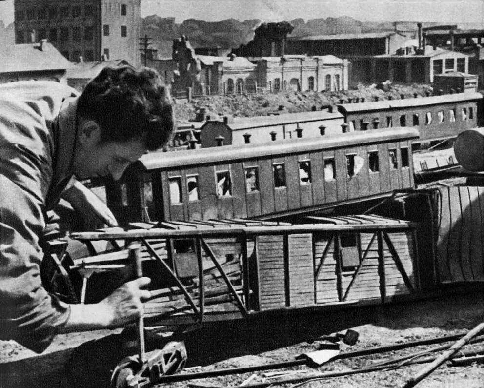 Пиротехник устанавливает пиротехнические заряды на макете разрушенной железнодорожной станции. Здания на фоне - тоже макеты.