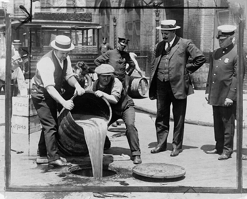 ЗАМЕСТИТЕЛЬ КОМИССАРА ПОЛИЦИИ НЬЮ-ЙОРКА ДЖОН А. ЛИЧ (СПРАВА) НАБЛЮДАЕТ, КАК АГЕНТЫ СЛИВАЮТ СПИРТНЫЕ НАПИТКИ В КАНАЛИЗАЦИЮ ПОСЛЕ РЕЙДА ВО ВРЕМЯ ЗАПРЕТА, 1921 год.