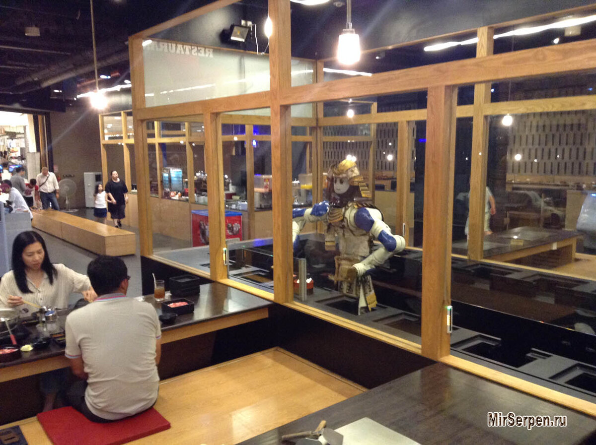 Японец разглядывает робота, а в это время японка забирает еду с его тарелки ))